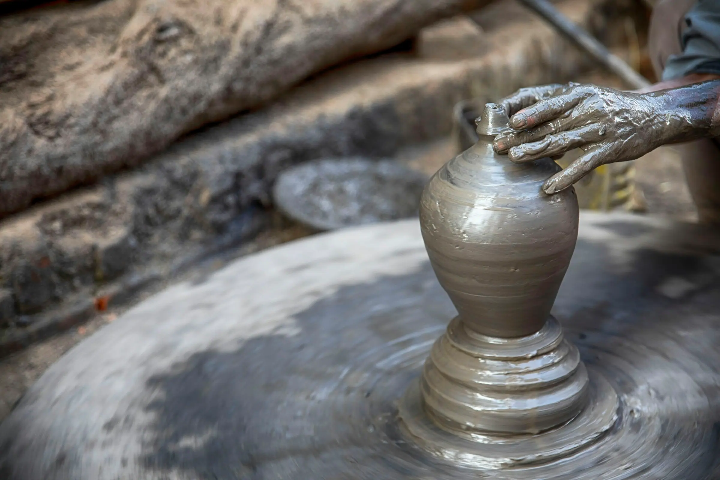 A potter's clay-covered hand shapes a vase on a spinning wheel.
