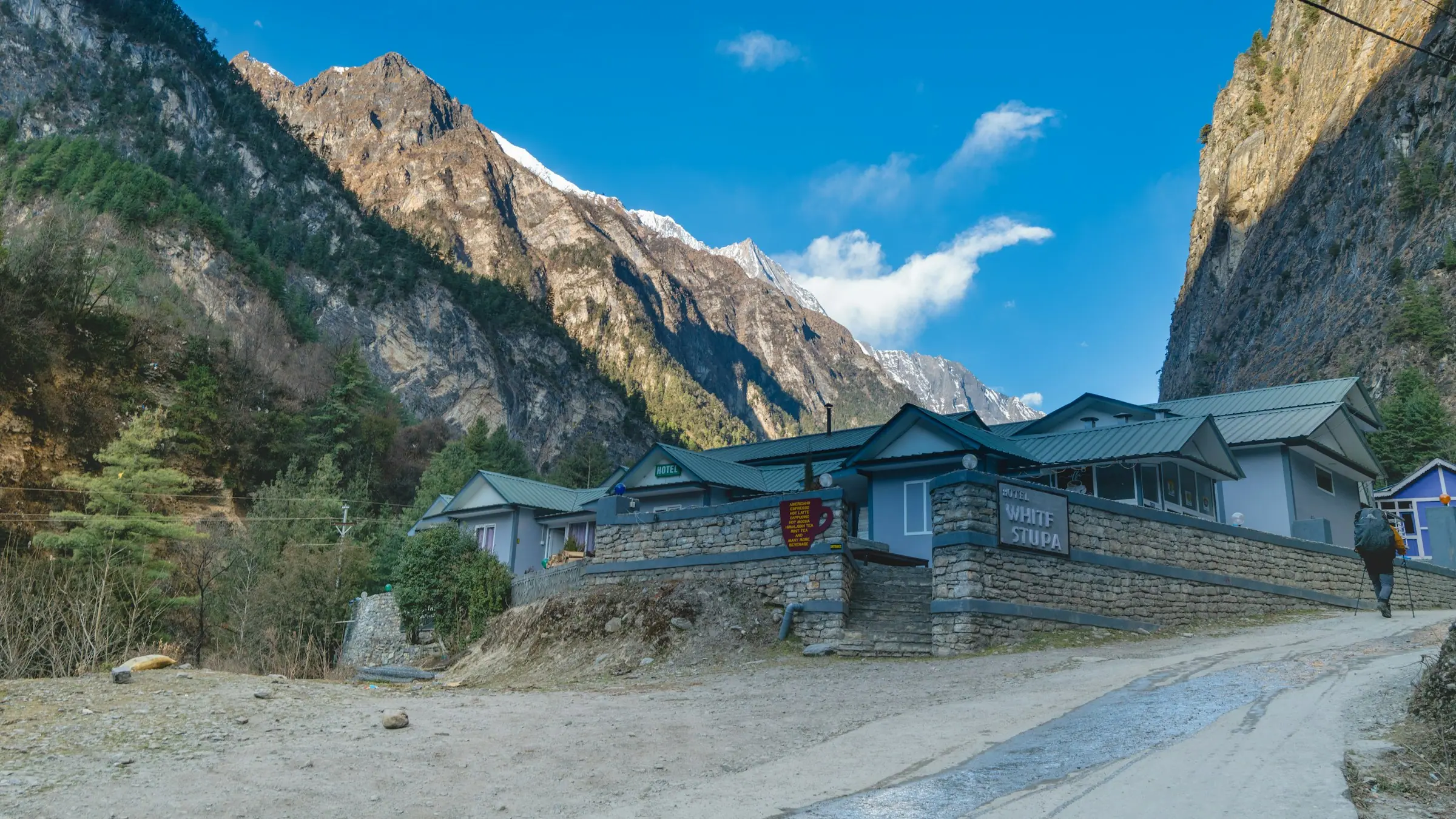 A stone-built mountain guesthouse with a green roof below steep forested slopes.